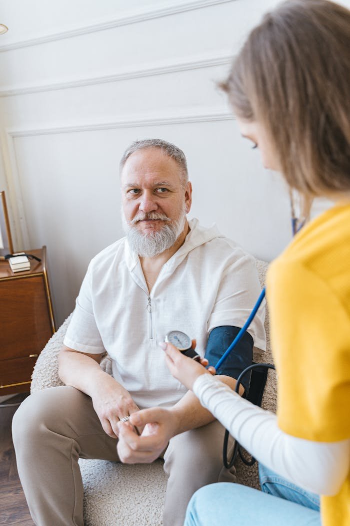 Offerings A healthcare worker takes the blood pressure of an elderly man using a monitor in a cozy indoor setting.
